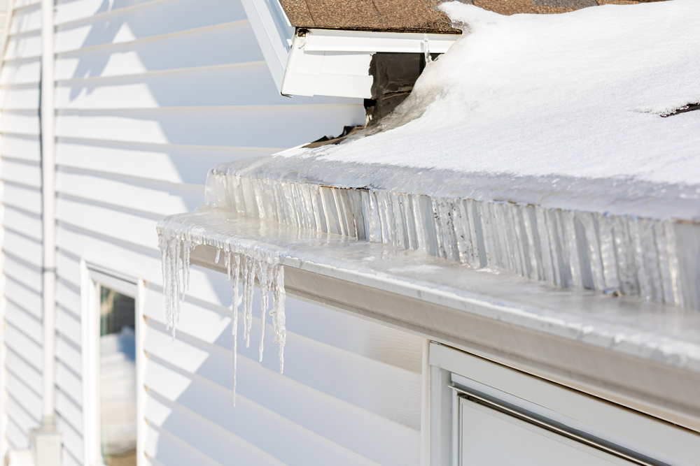 Icicles on gutter of house with snow on roof