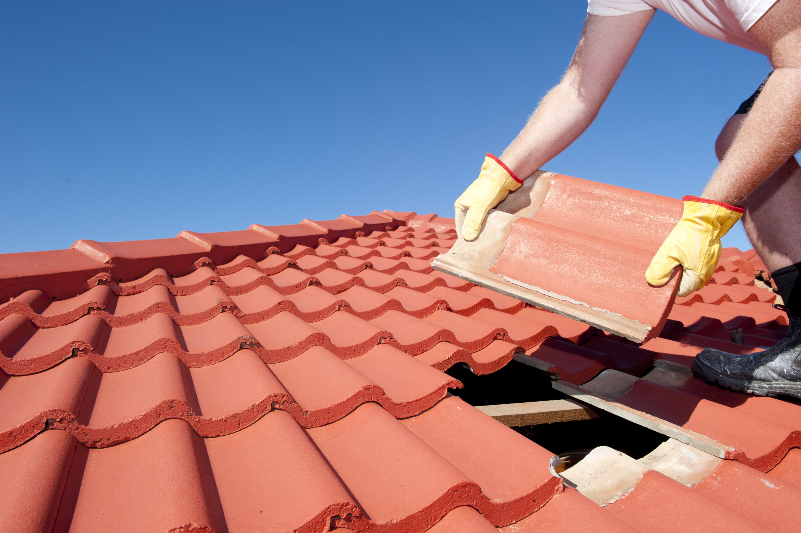 person with yellow gloves placing red tiles on gap in roof